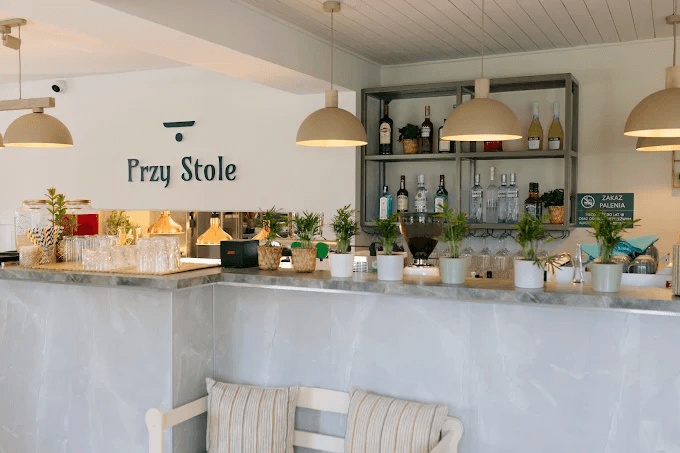 Bar restauracji Przy Stole z logo na ścianie i rzędem doniczek z ziołami